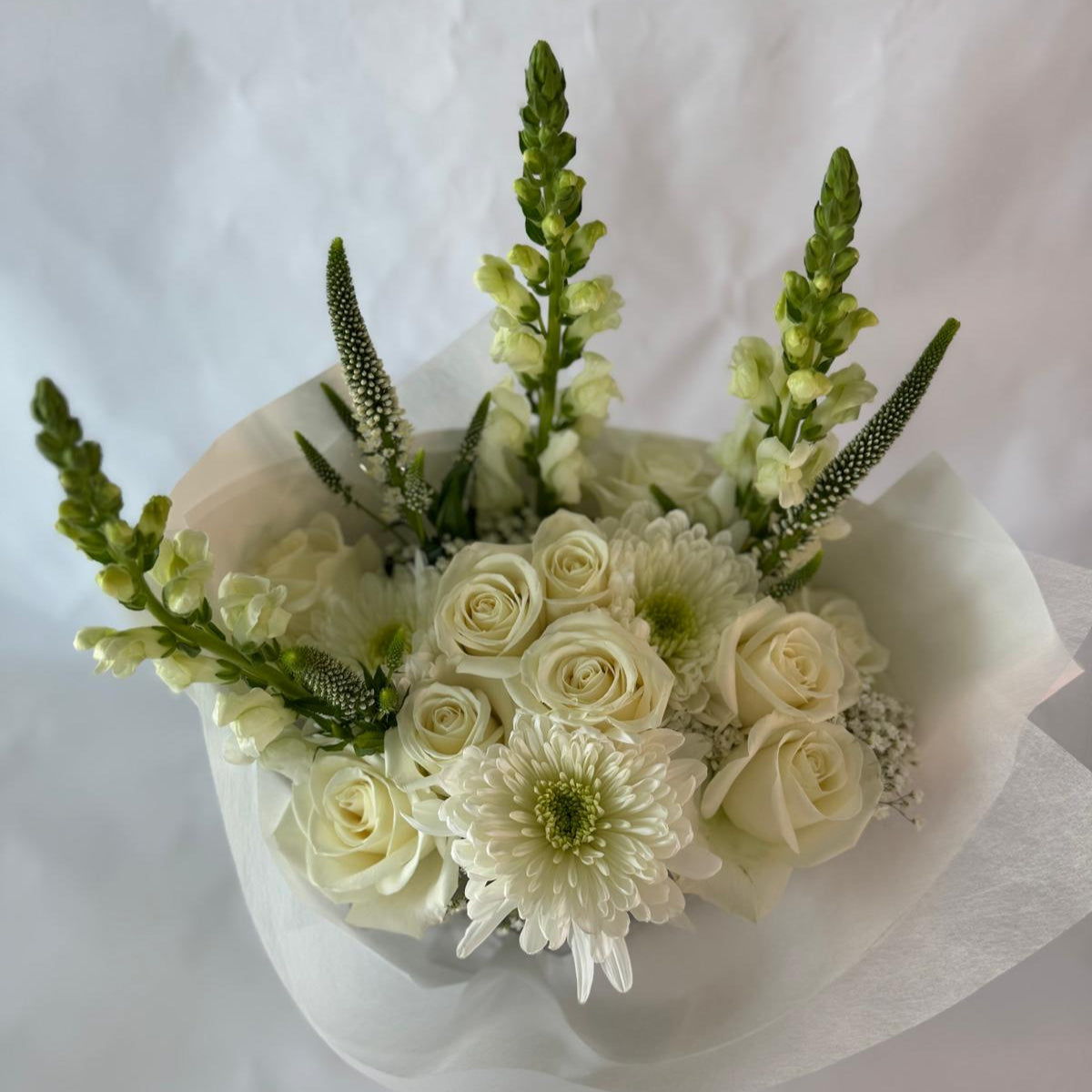 An elegant all-white bouquet wrapped in sheer white paper, symbolizing peace, purity and everlasting light, offered as a gentle tribute in times of remembrance.