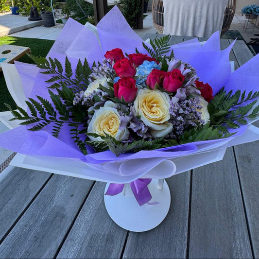 October Radiance bouquet inspired by opal and pink tourmaline, featuring jewel-toned and pastel blooms wrapped in lilac and white for a radiant autumn design.