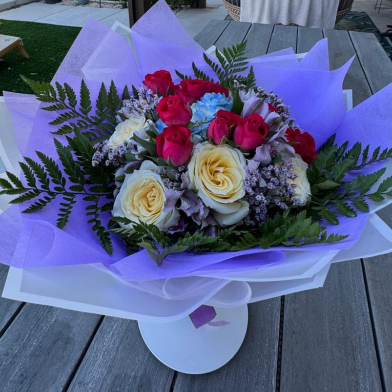 October Radiance bouquet inspired by opal and pink tourmaline, featuring jewel-toned and pastel blooms wrapped in lilac and white for a radiant autumn design.