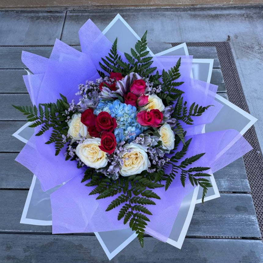 October Radiance bouquet inspired by opal and pink tourmaline, featuring jewel-toned and pastel blooms wrapped in lilac and white for a radiant autumn design.