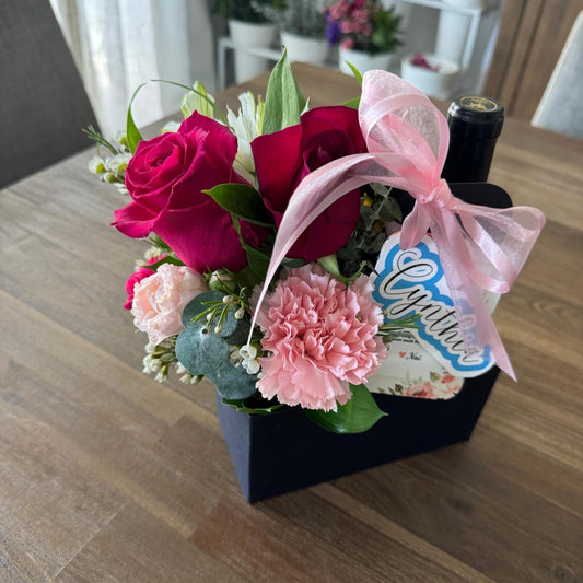 Custom floral party favor in a gift carrier with roses, carnations, and ribbon.