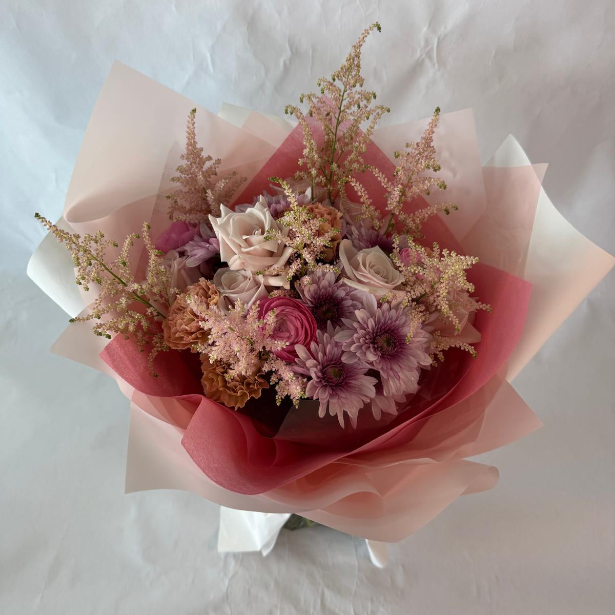 A gentle bouquet in warm blush and rose tones, softly wrapped in pink and cream, offering warmth and compassion during moments of grief.