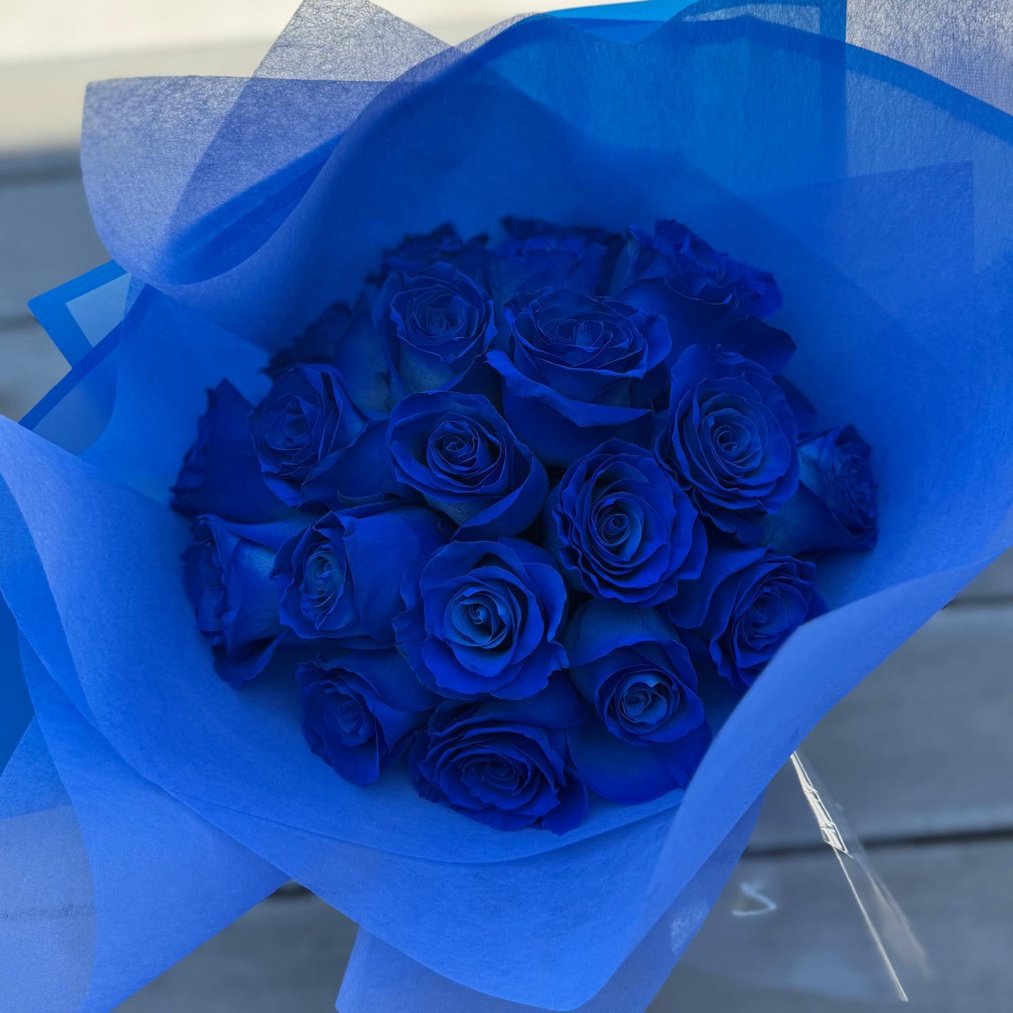 Hand-tied bouquet of deep sapphire-blue roses wrapped in blue matte paper with a satin ribbon.