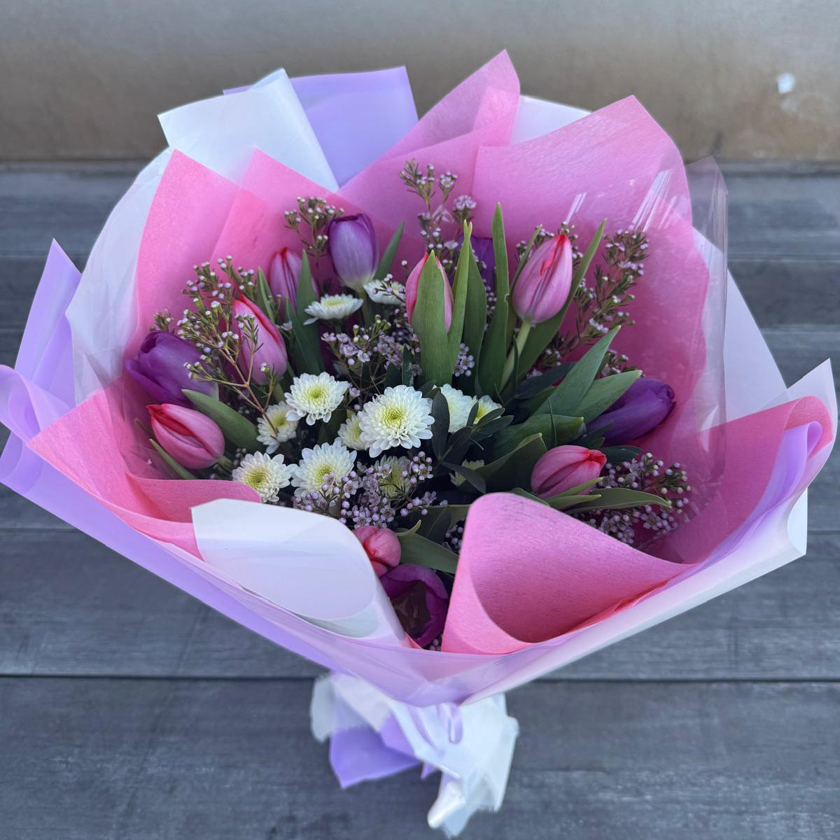 Spring bouquet with pink and lavender tulips, white chrysanthemums, and wax flower wrapped in blush and lilac pastel paper.