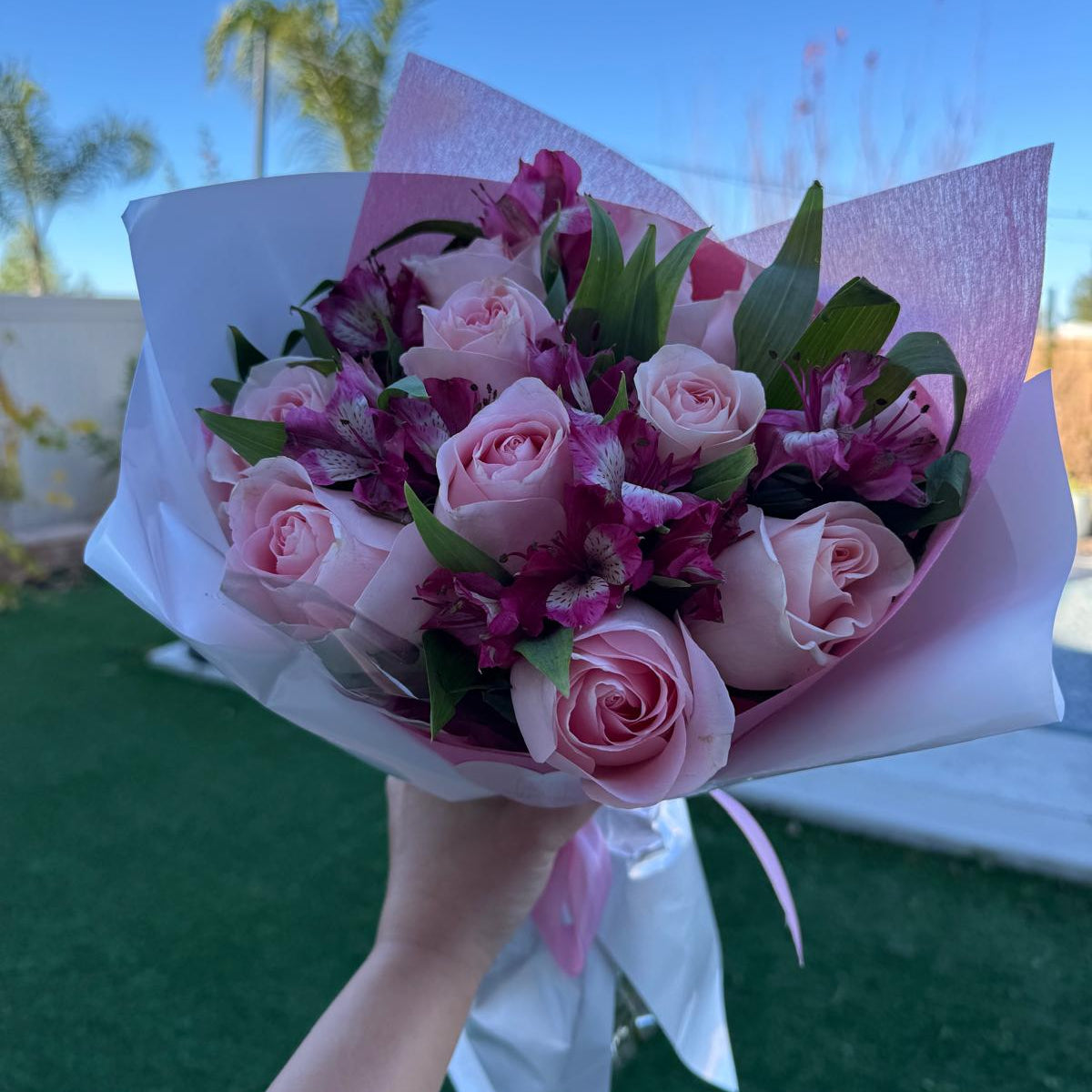 Blushing Grace Bouquet in one size only featuring blush pink roses and magenta alstroemeria wrapped in pink and white paper with satin ribbon by Nai Pascoal Bouquets